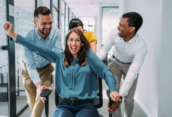 Group of cheerful creative business colleagues having fun during chair race in modern office.