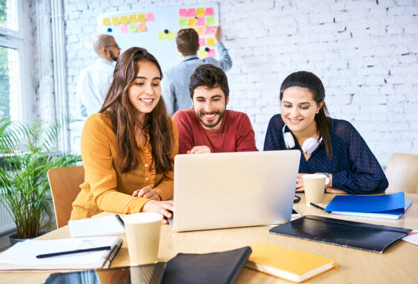 Group of young creative workers looking at laptop and brainstorming during meeting. University students studying together