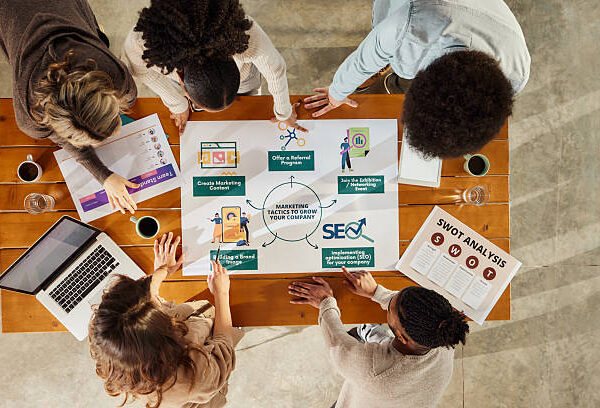High angle view of team of creative people cooperating while analyzing marketing tactics for expanding a company in the office.