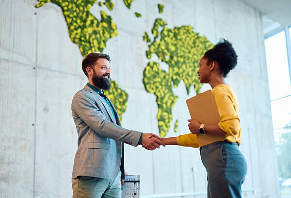 Two business partners shaking hands after a successful meeting in a modern office with a green world map, symbolizing global partnership and sustainability