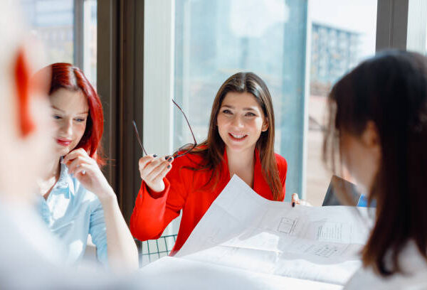 Experience the positivity and collaboration in a modern office with this engaging stock photo, featuring a female manager, two young female creative employees, a young working man in a vest, and a middle-aged general manager having a fun and positive meeting. They are sitting at the table in a modern office, engaged in conversation. The office's large windows allow sunlight to shine through, creating a bright and uplifting atmosphere. Ideal for conveying teamwork and positive workplace culture, this photo is perfect for business-related promotions, team-building publications, and social media content celebrating effective collaboration in a contemporary office. Positive office meeting, Manager, Creative team, Modern office, Collaboration, Teamwork, Sunlight, Large windows, Positive workplace culture, Stock photo, iStock, Business-related promotions, Team-building publications, Social media, Effective collaboration, Contemporary office.